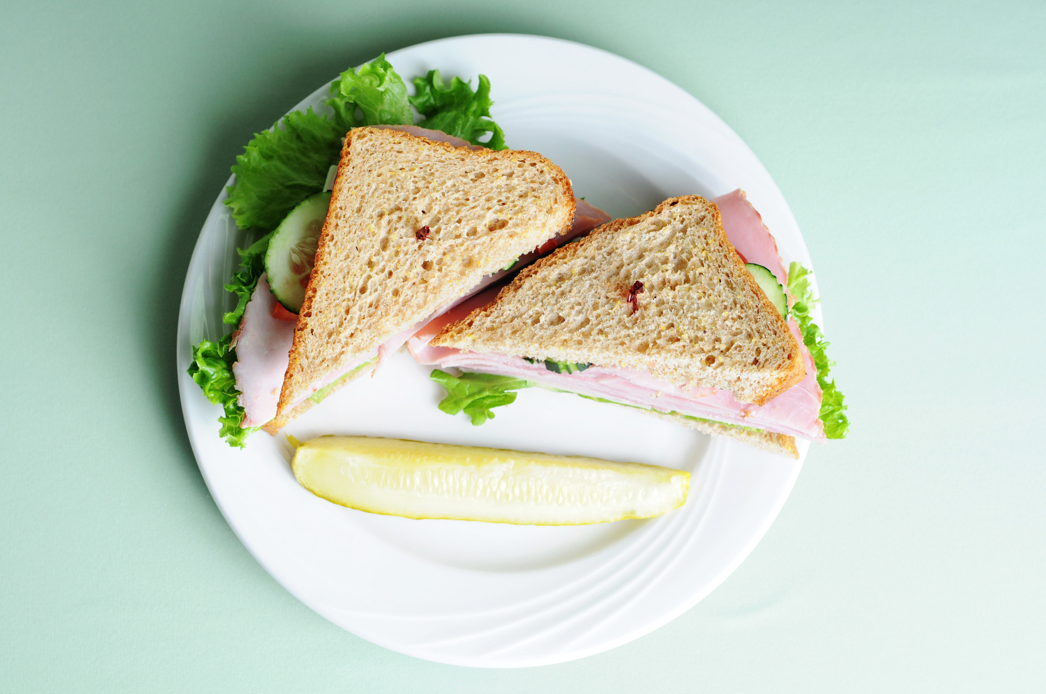 A sliced ham sandwich with a pickle on the side.