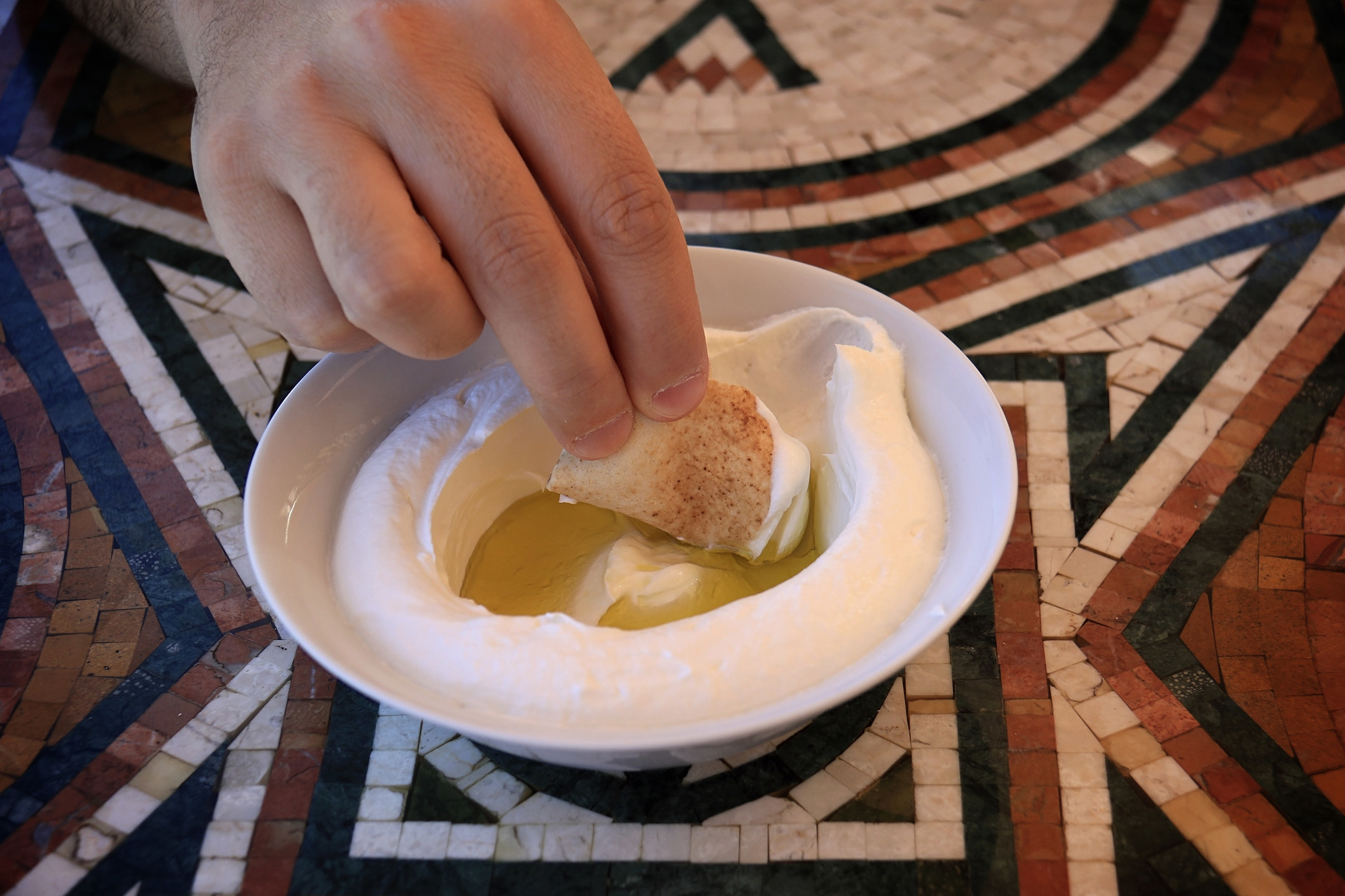 A man dipping a pita bread slice in labneh and olive oil.
