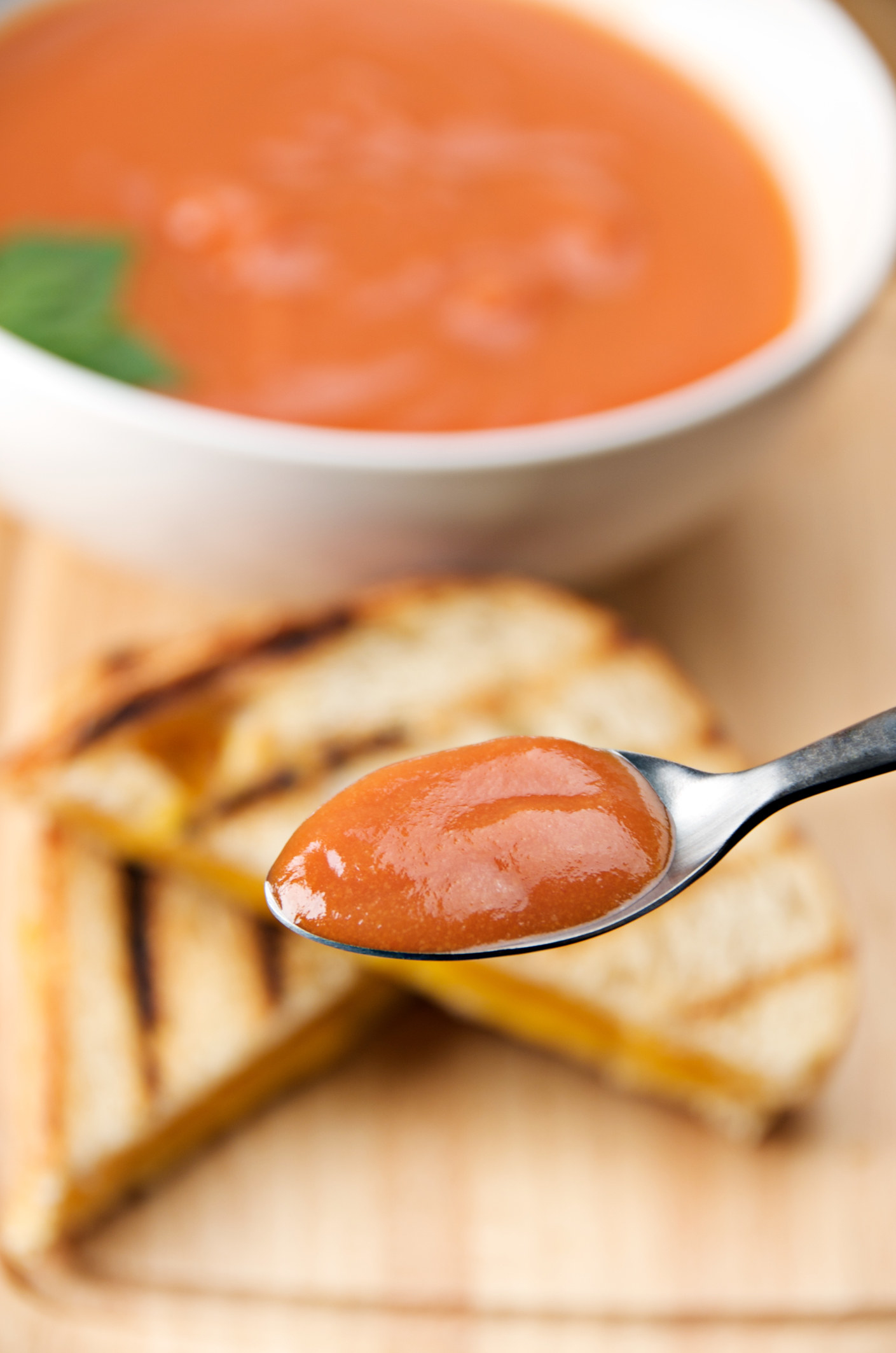 Spoon of tomato soup close-up with grilled cheese and bowl of tomato soup