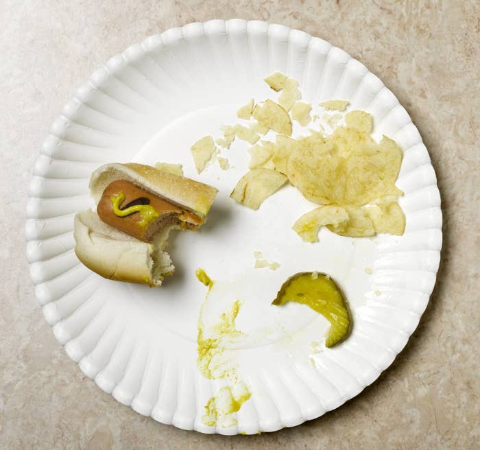 An eaten hot dog with potato chips and a pickle.