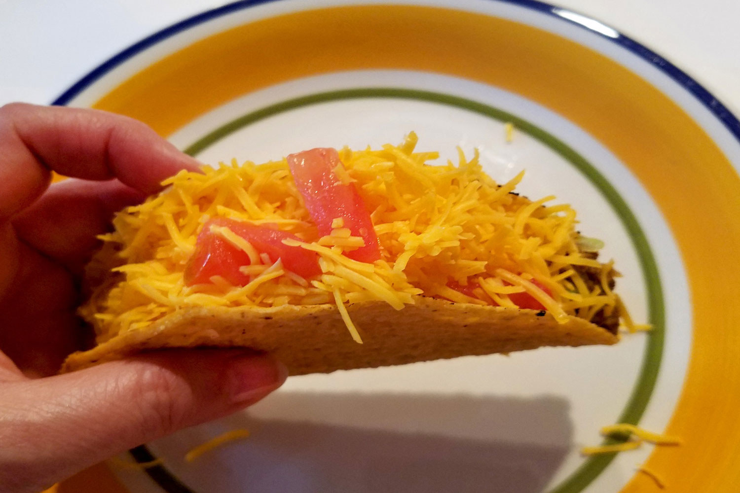 A hard taco filled with beef, cheese, and tomato.