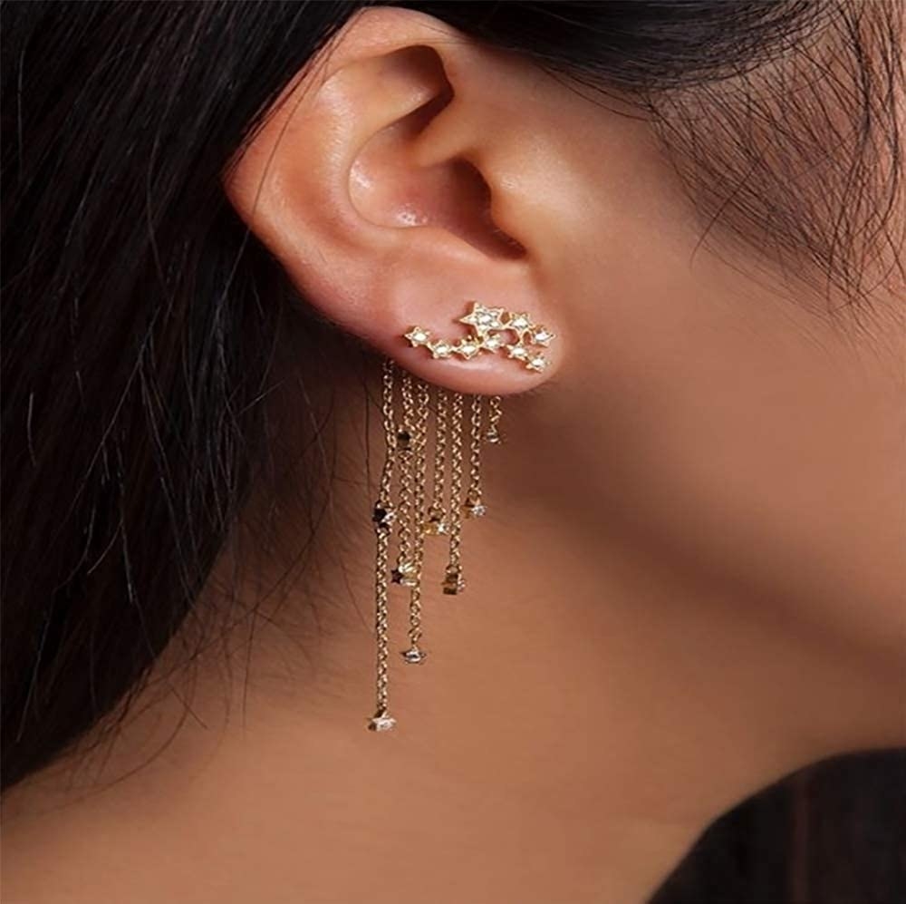 model wearing the gold and rhinestone earrings with constellation shaped studs and backs with chain fringe and matching star charms