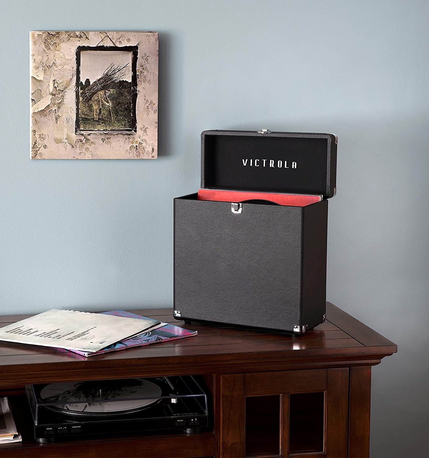 A storage box propped open with records inside on top of a table with a record player underneath, and a record on the wall