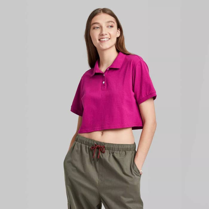 Model wearing magenta polo with collar, stops above belly button