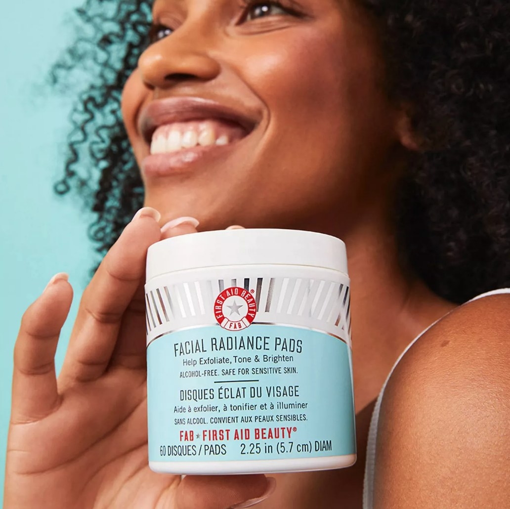 A model holding a container of exfoliating, toning, and brightening facial pads