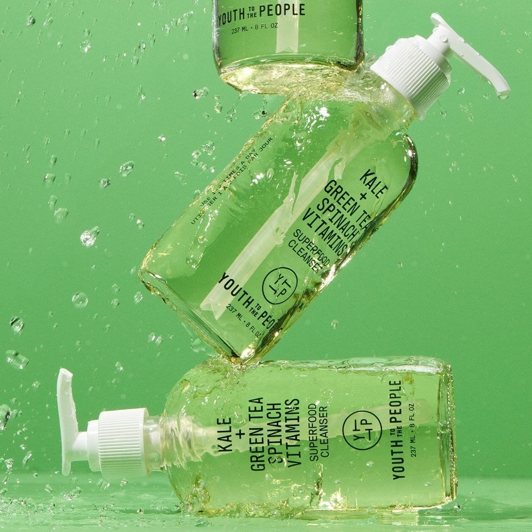 A trio of facial cleansers in transparent glass bottles covered in water
