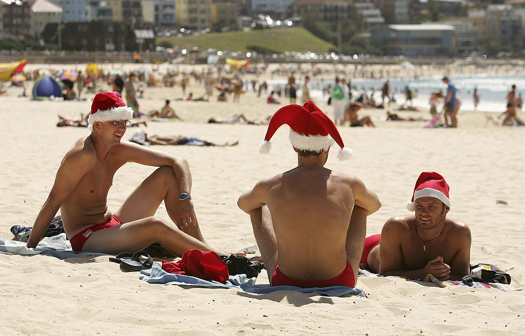 A trio of men at the beach wearing matching Speedos and Santa hats