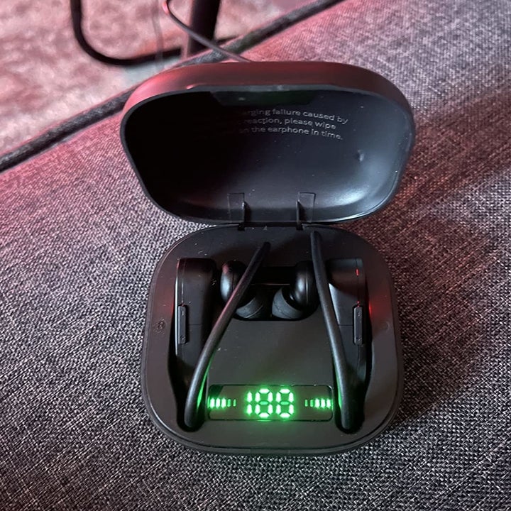 Reviewer image of black wireless earbuds in charging case with charge percentage displayed