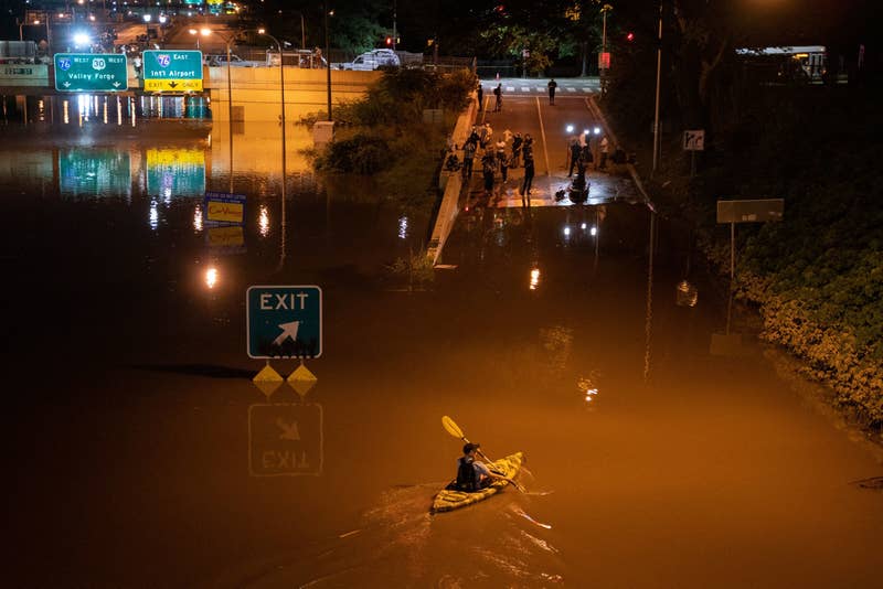 A man kayaks on a flooded roadway while a group of people watch 
