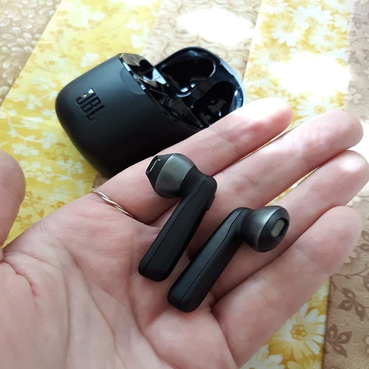 Reviewer holding black wireless earbuds next to charging case