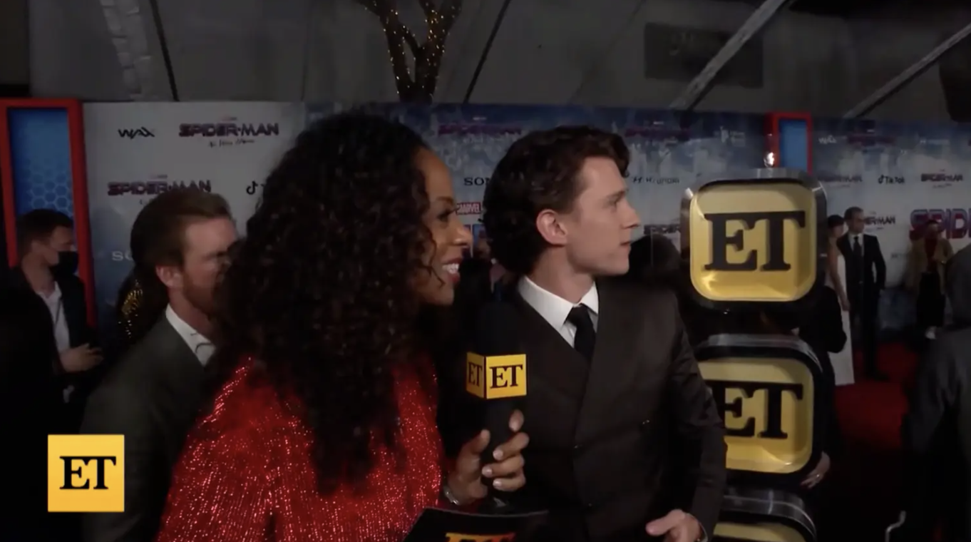 Tom Holland and interviewer looking at Zendaya arrive on the red carpet