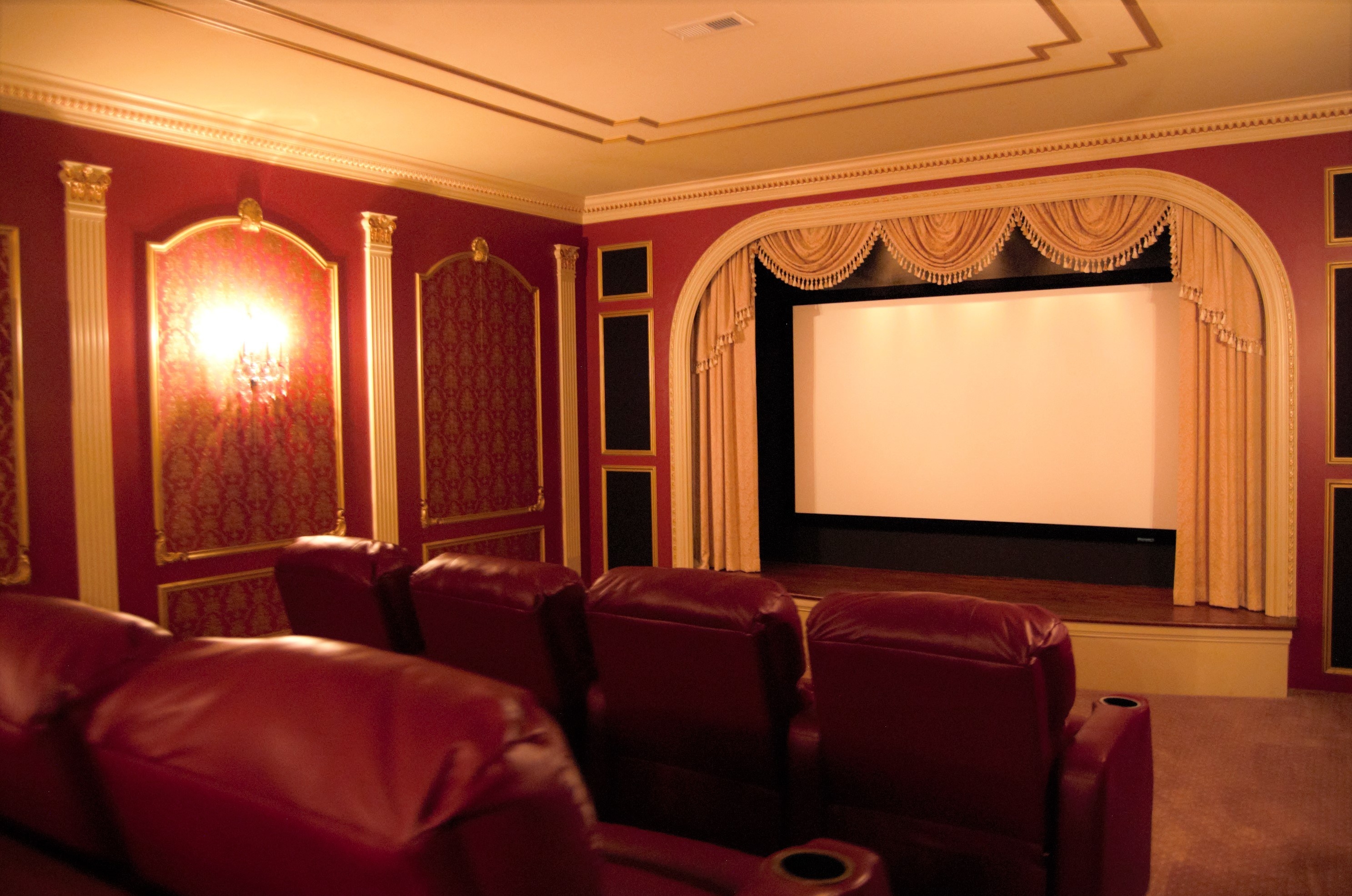 Red home theater with large red reclining chairs and a gold curtain around the projector screen