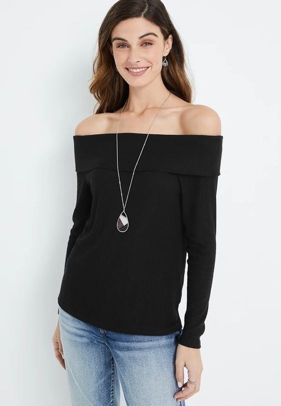 An image of a model wearing a black ribbed off-the-shoulder top