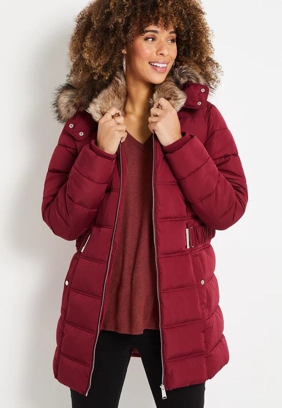 An image of a model wearing a red long puffer jacket with a hood