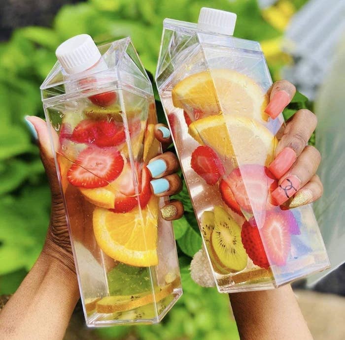two models hold the clear bottle with water and fruit inside
