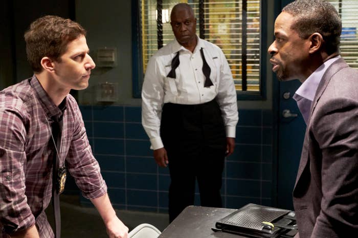Image shows Andy Samberg as Jake Peralta leaning over a table in a police interview room as he faces off with a suspect with Captain Holt in the background