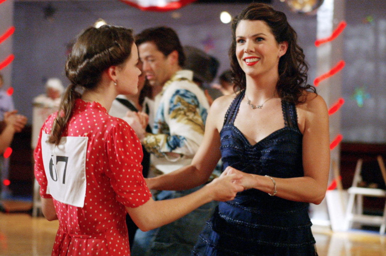Lorelai and Rory wear brightly coloured 1950s style dresses makeup and hair and dance together in a town hall in a still from Gilmore Girls