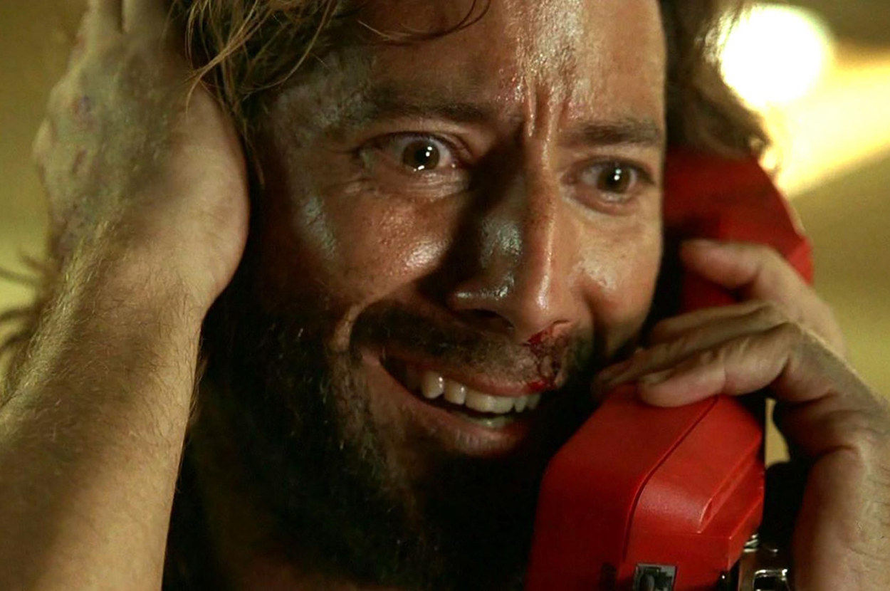 A man looks very relieved whilst pushing his hair out of his face and holding a big red phone to his ear