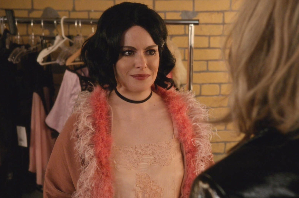 Stevie from Schitt&#x27;s Creek talks to Moira out of frame wearing a black wig and a fluffy pink 1920s style outfit