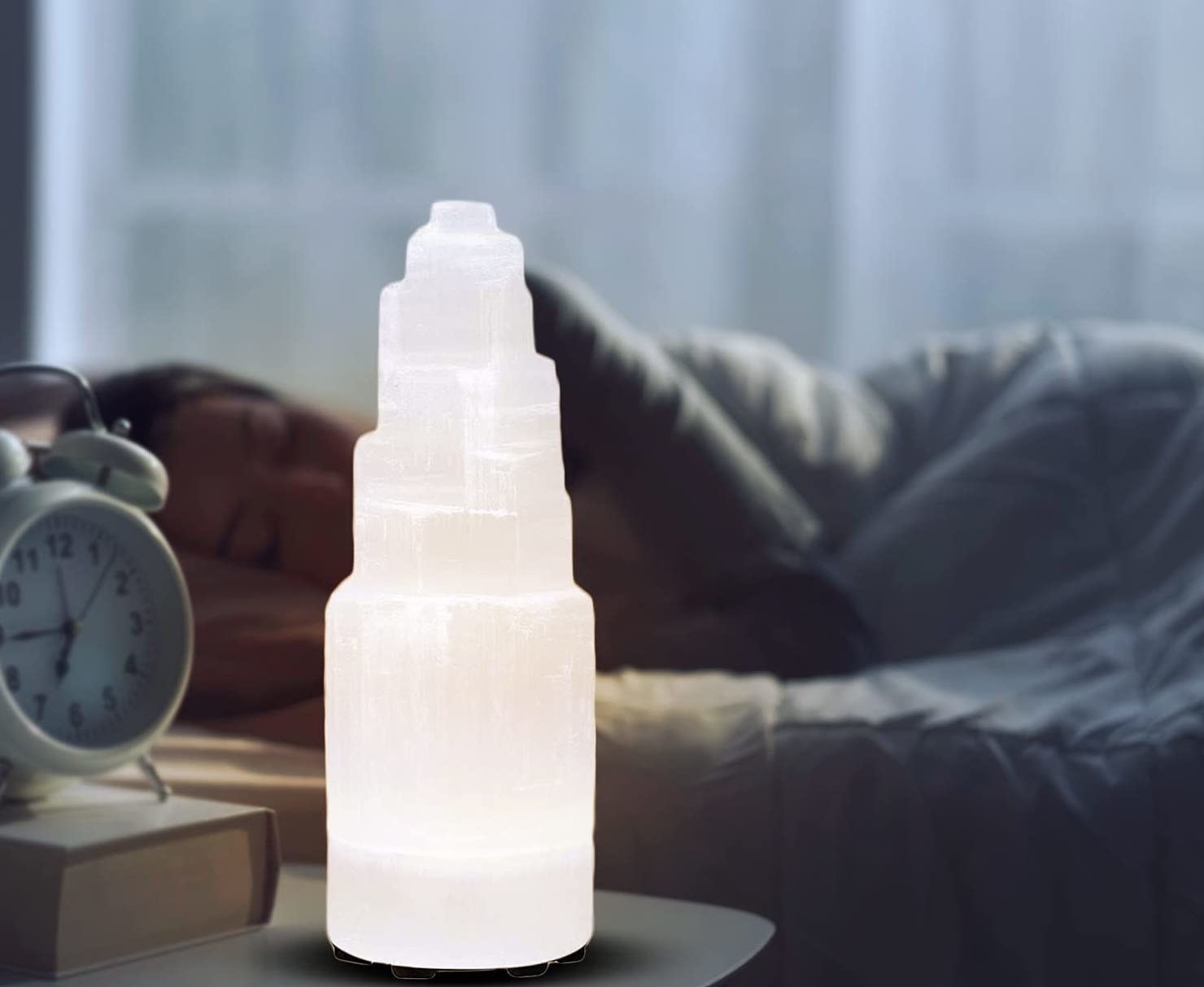 A selenite lamp on a bedside table in front of a person sleeping