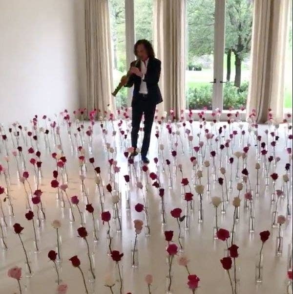 Kenny G performing in a room that has dozens of single roses in individual vases on the floor
