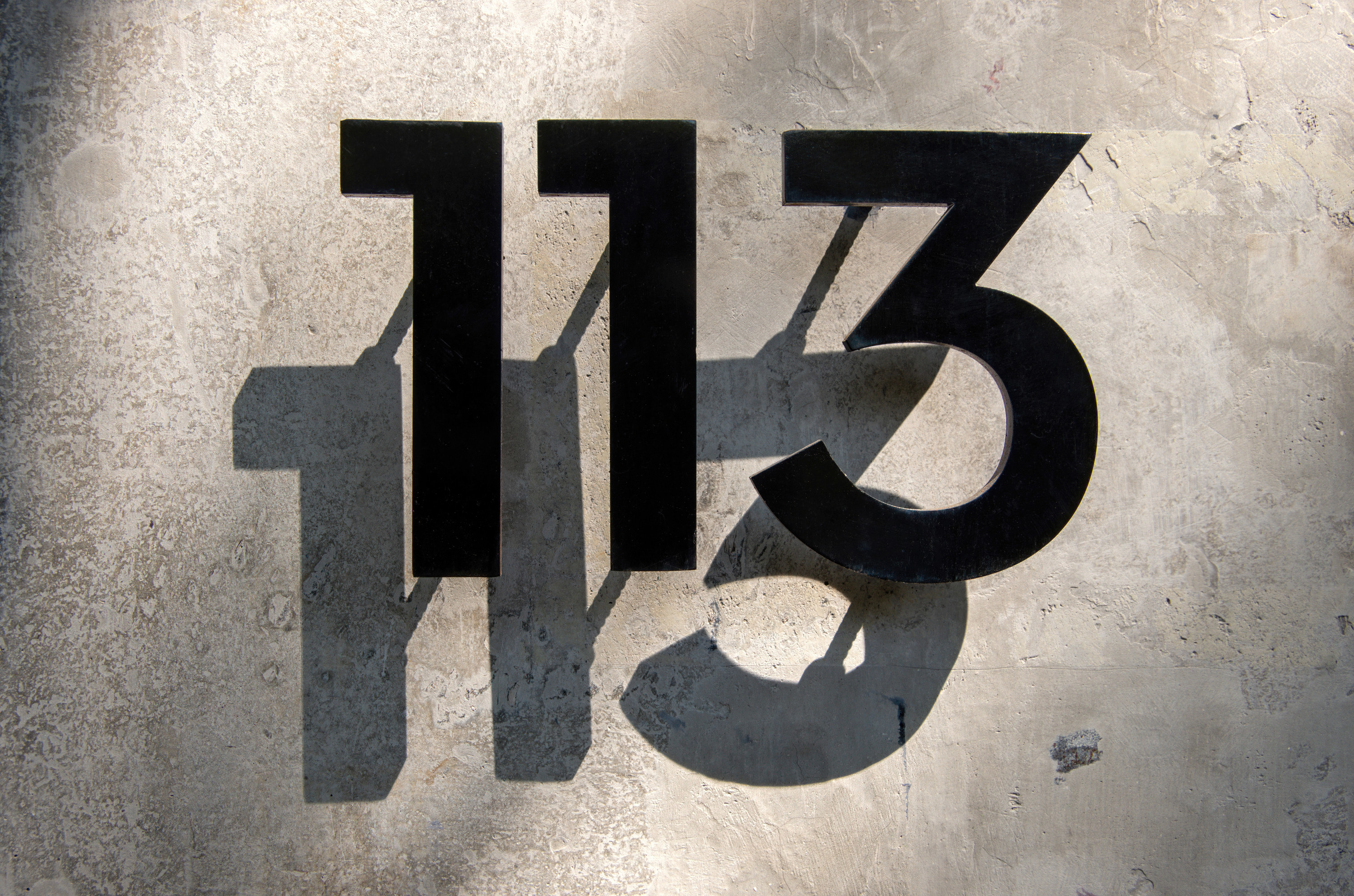 Metal house number &quot;113&quot; in front of a concrete wall