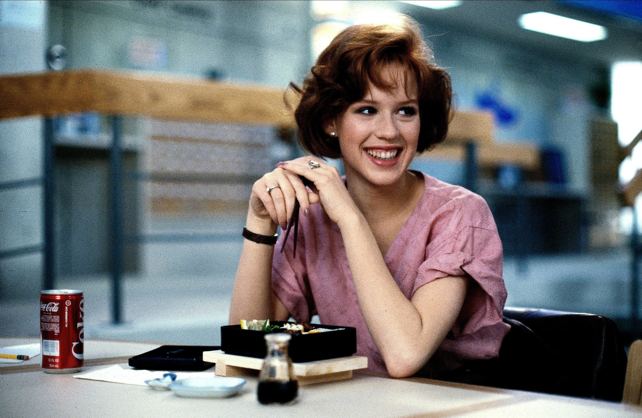 Molly Ringwald smiling with chop sticks in her hand during filming for the movie titled the breakfast club