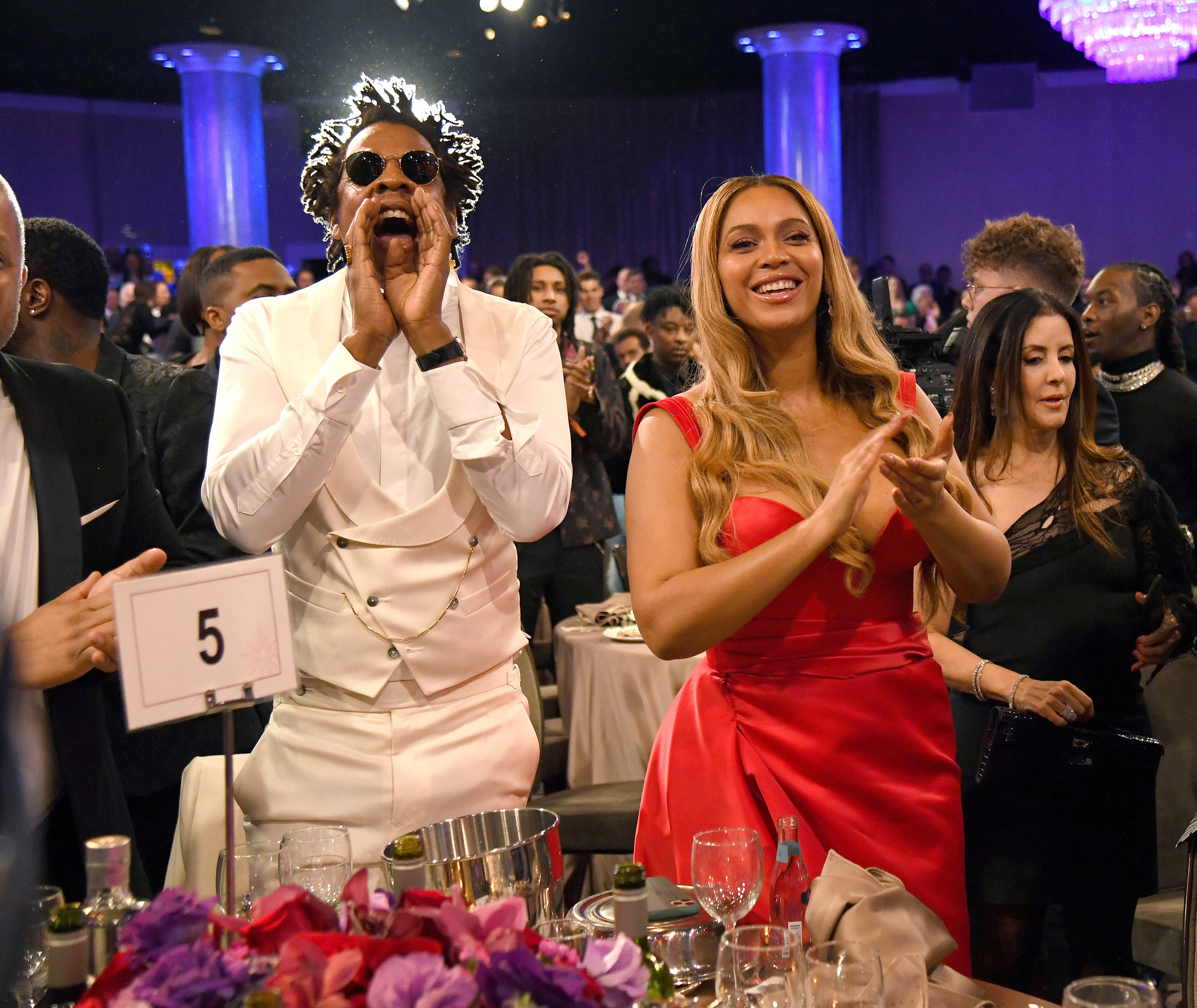 Jay-Z and Beyoncé cheer while standing beside a table at an event