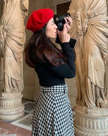 Reviewer wearing the red beret with a black top and houndstooth skirt while taking a photo