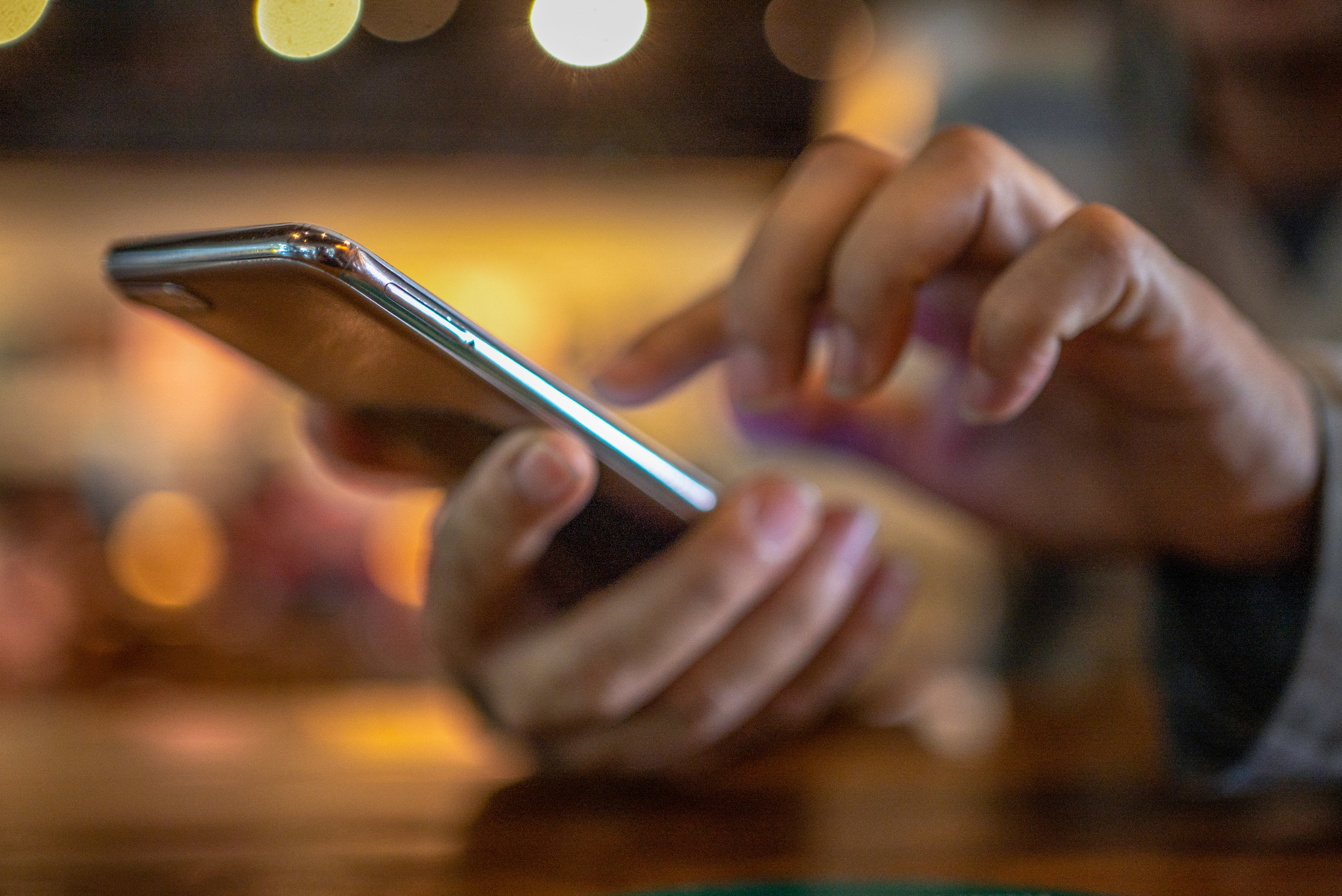 A man holding a smartphone with coffee cup on wooden table in cafe