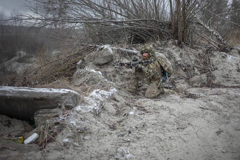 A person in fatigues crouched on the ground