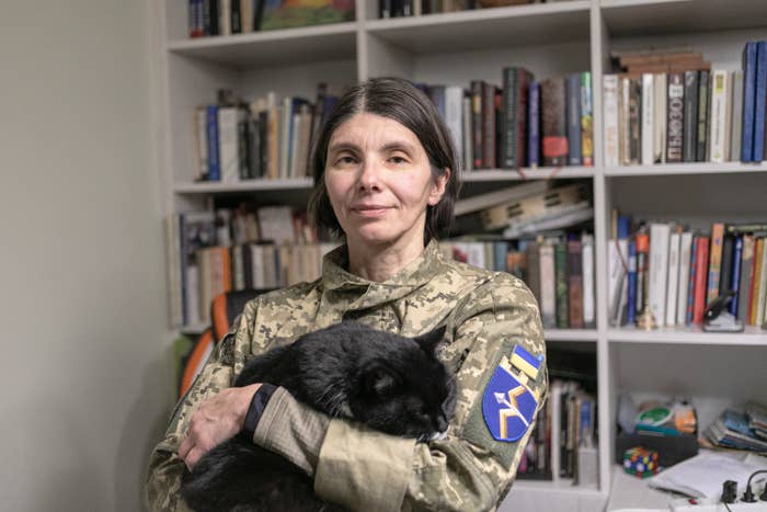 A woman in fatigues holding a cat in a home office