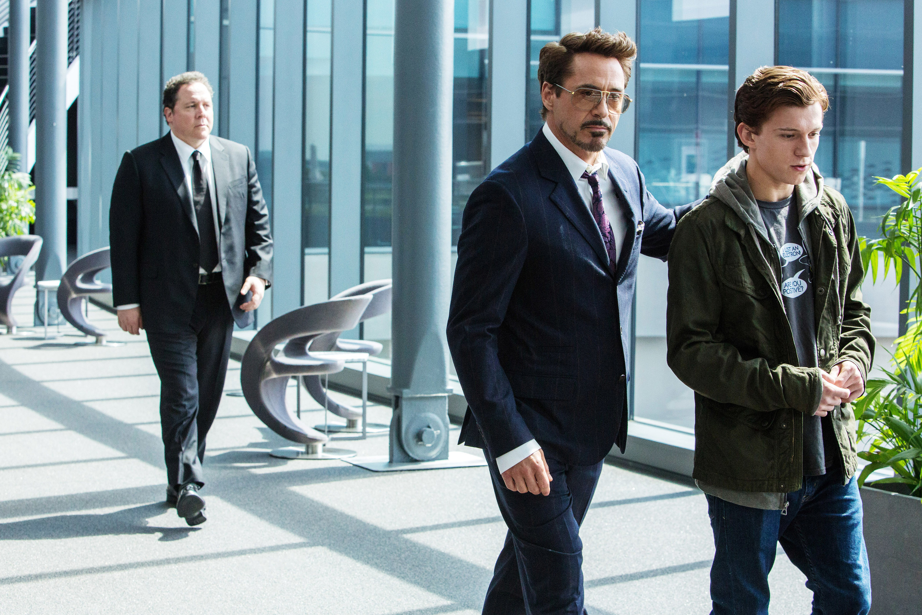 Iron Man pats Spider-Man on the back while Happy Hogan walks behind them
