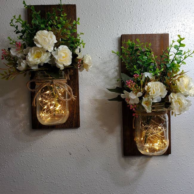 two mason jars mounted on wood with lights inside and florals int he top