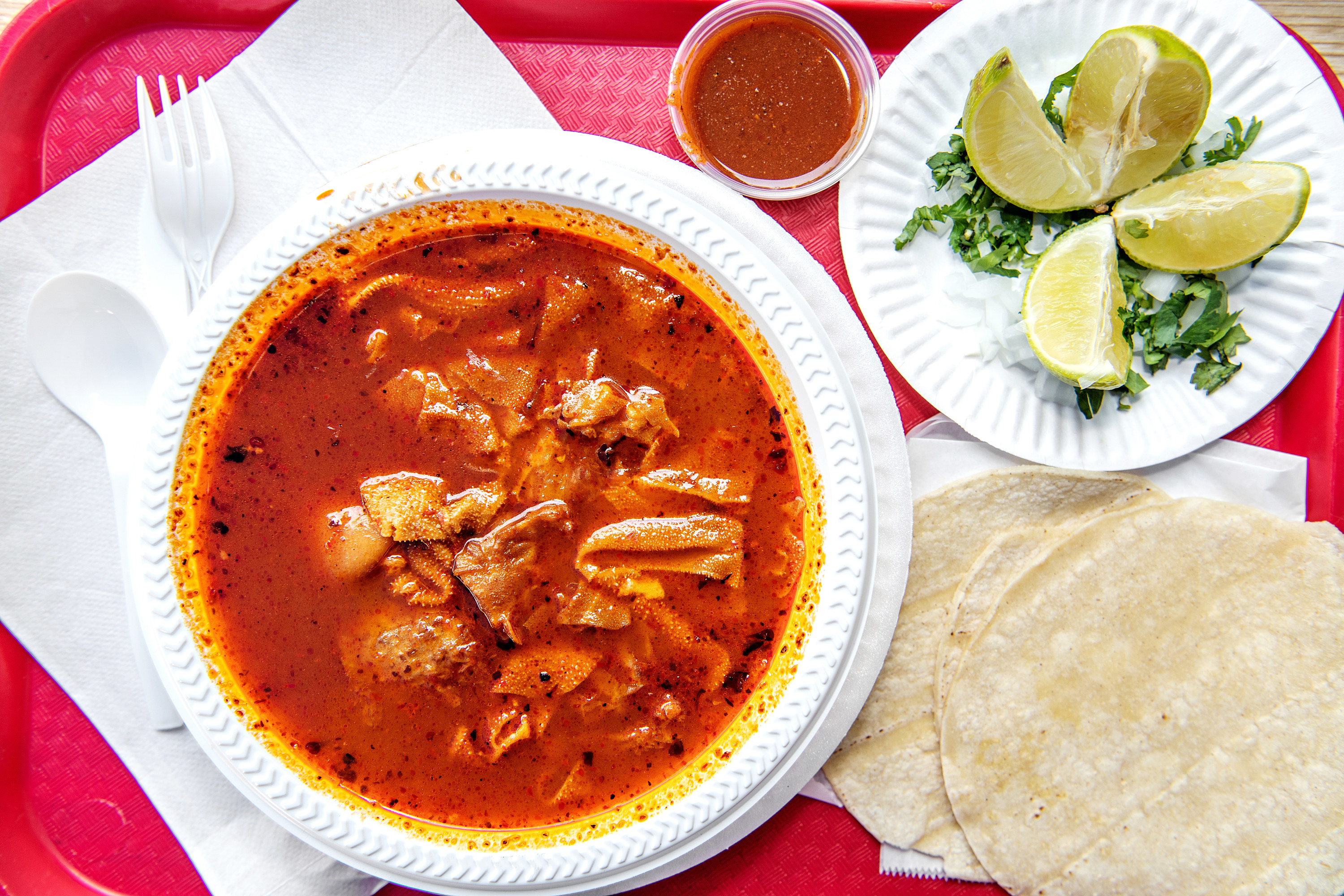 Bowl of menudo with lime wedges and tortillas