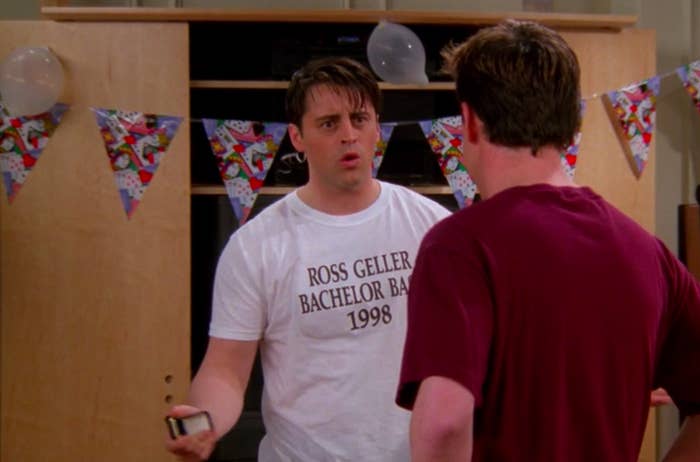 Joey wearing a Ross Geller Bachelor Bash 1998 T shirt in front of some condom balloons