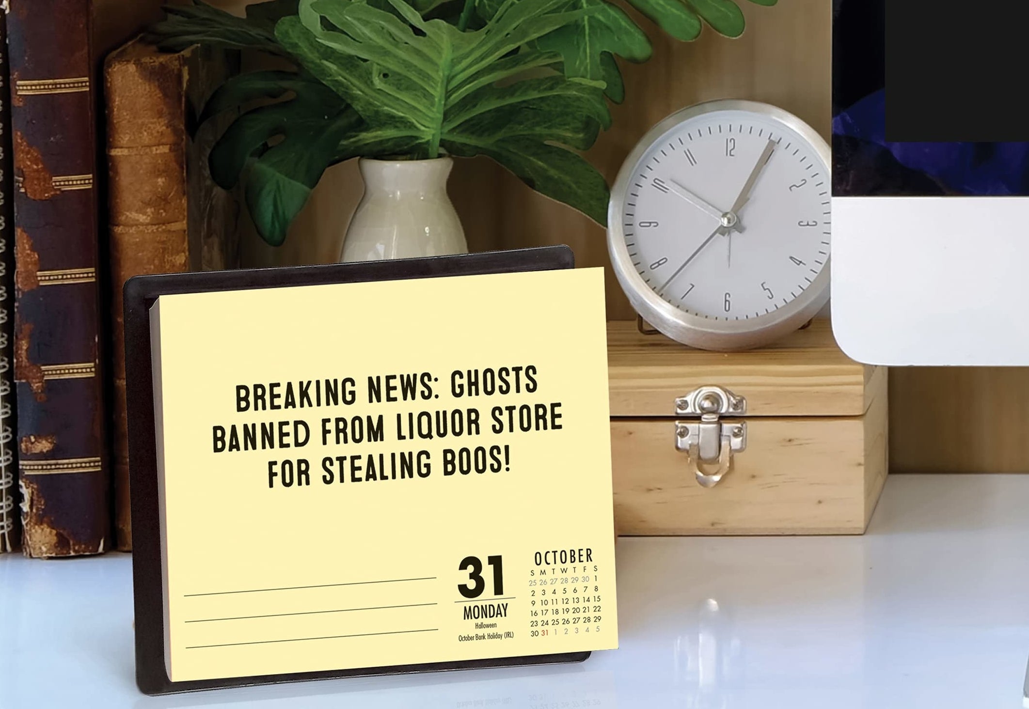 The pun calendar on a desk with the date October 31. it says &quot;breaking news: ghosts banned from liquor store for stealing boos!&quot;