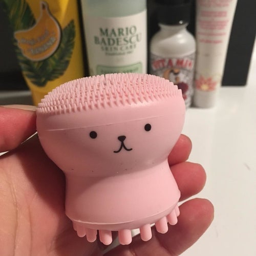 a reviewer holds the pink cleansing brush up, showing the cute face in front