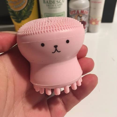 a reviewer holds the pink cleansing brush up, showing the cute face in front