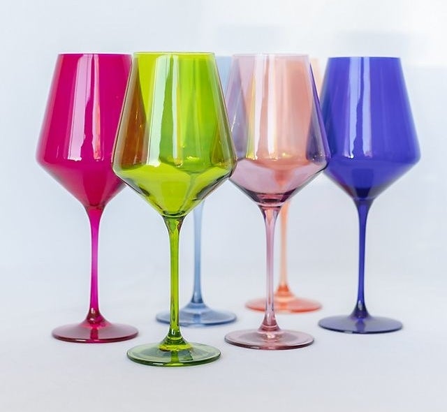 Six wine glasses; one in blue, purple, orange, green, yellow, and pink