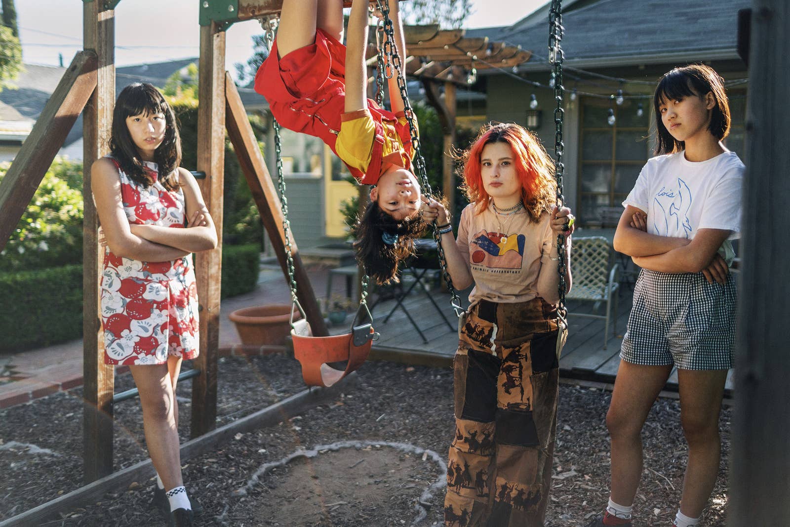 Three girls on a swingset while one hangs upside down from the top bar 