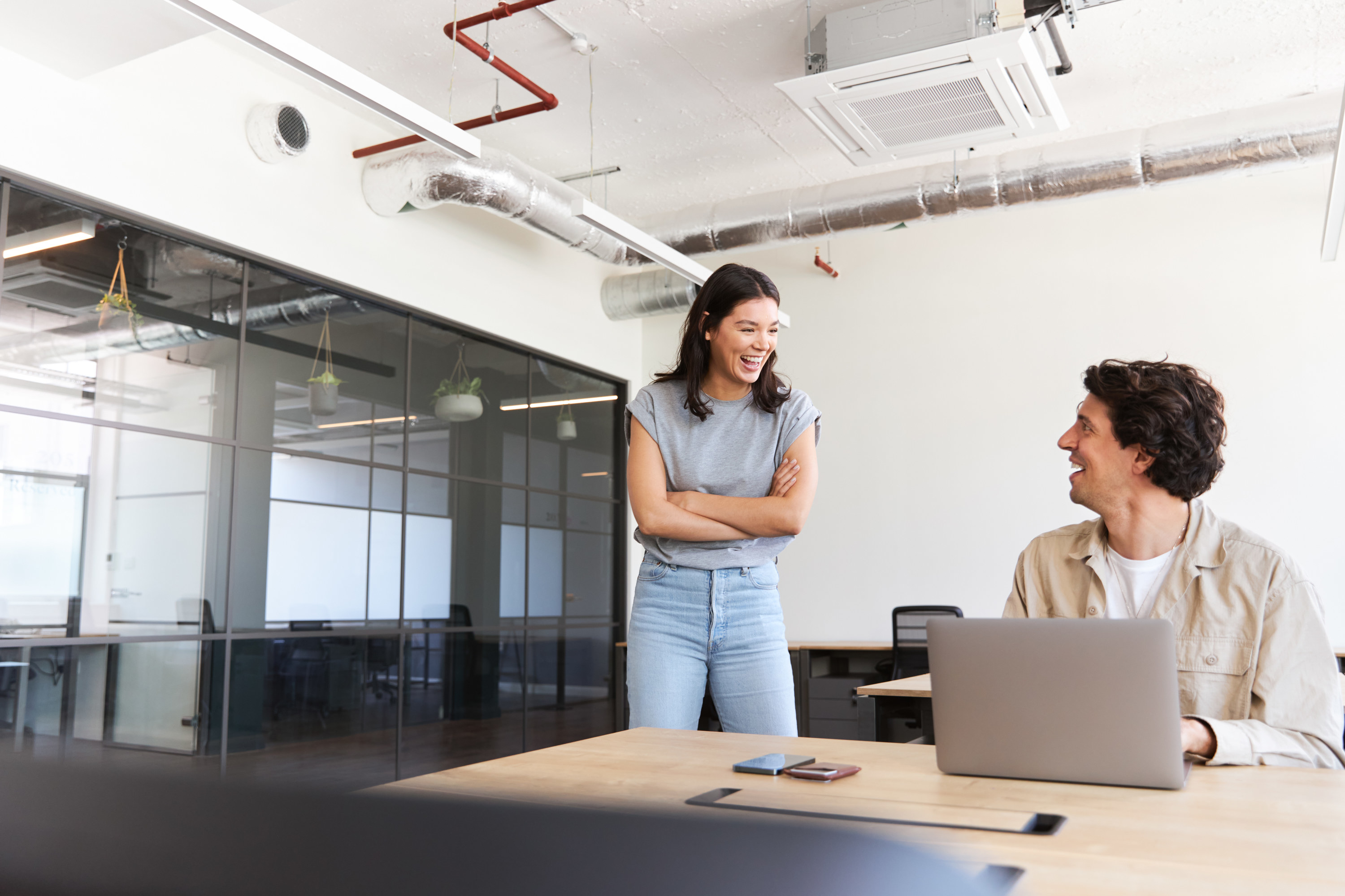 Man and woman working in an office standing by desk and flirting