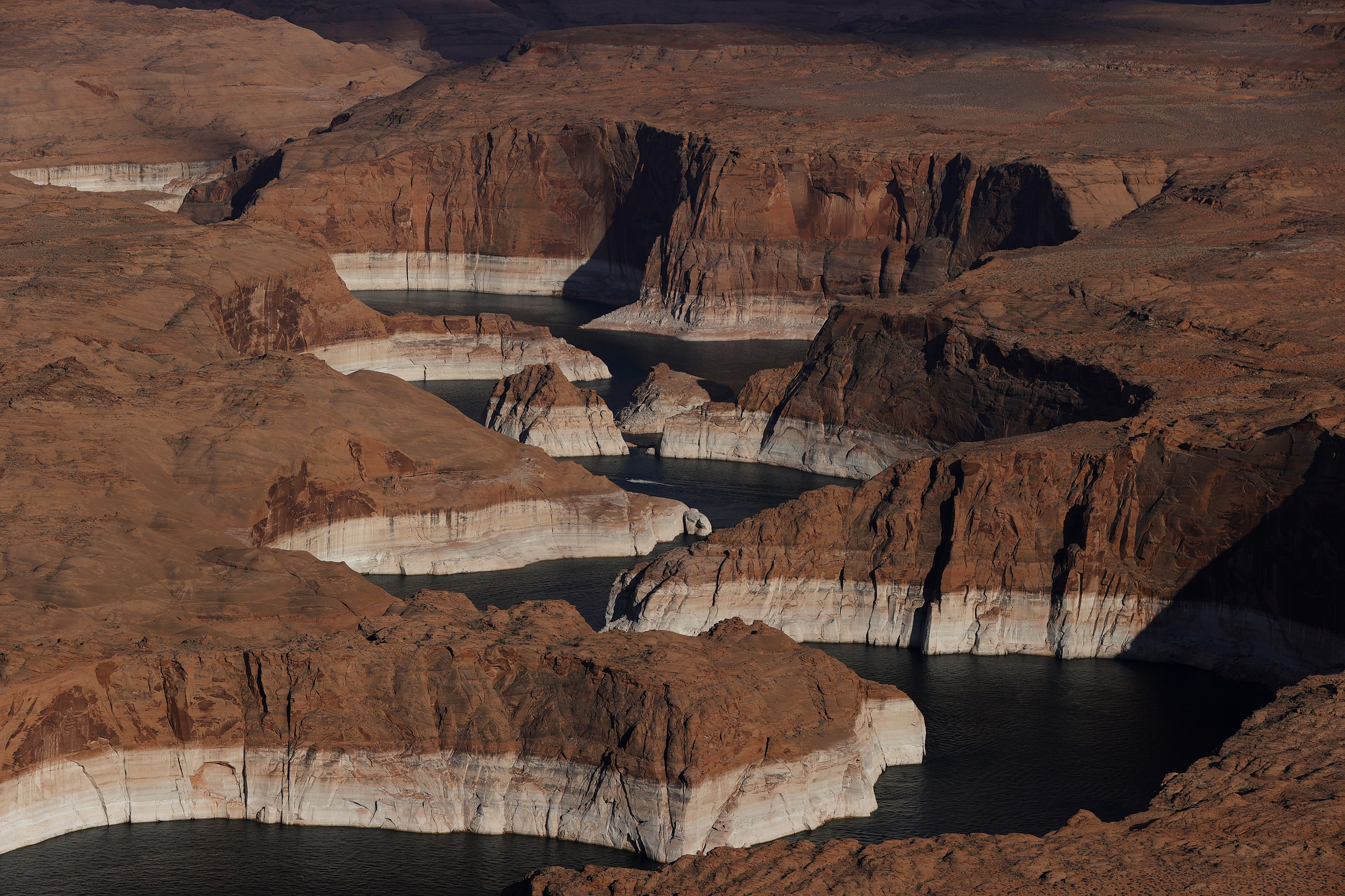 A river snakes through some rocks on Lake Powell with two stripes in the rock showing the high water mark 