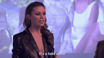 A woman gestures to her face and says