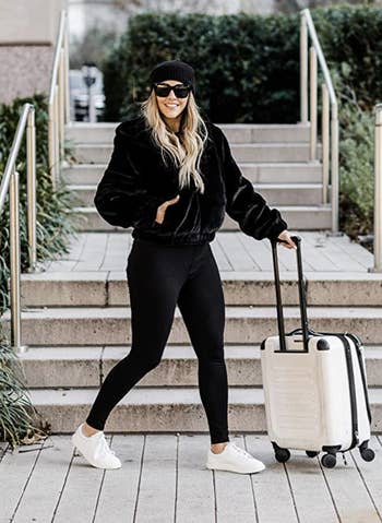 model walking with suitcase in black faux fur bomber jacket