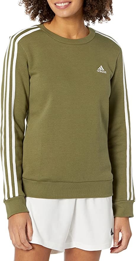 model in shorts and an olive green sweatshirt with three adidas stripes down the sleeves