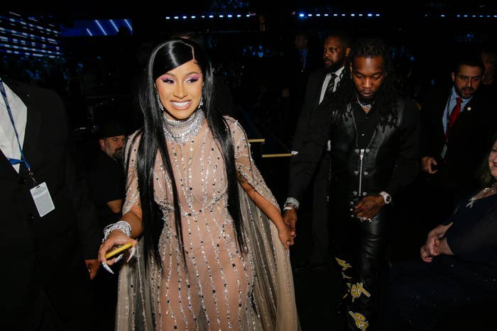 Cardi smiling widely as she walks hand-in-hand with Offset through a crowd of people
