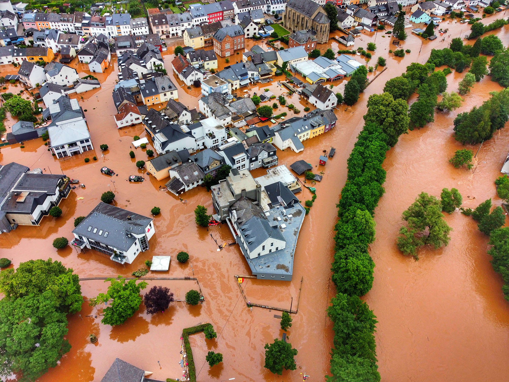 An aerial shot of a german village flooded with brown water with houses and trees above it