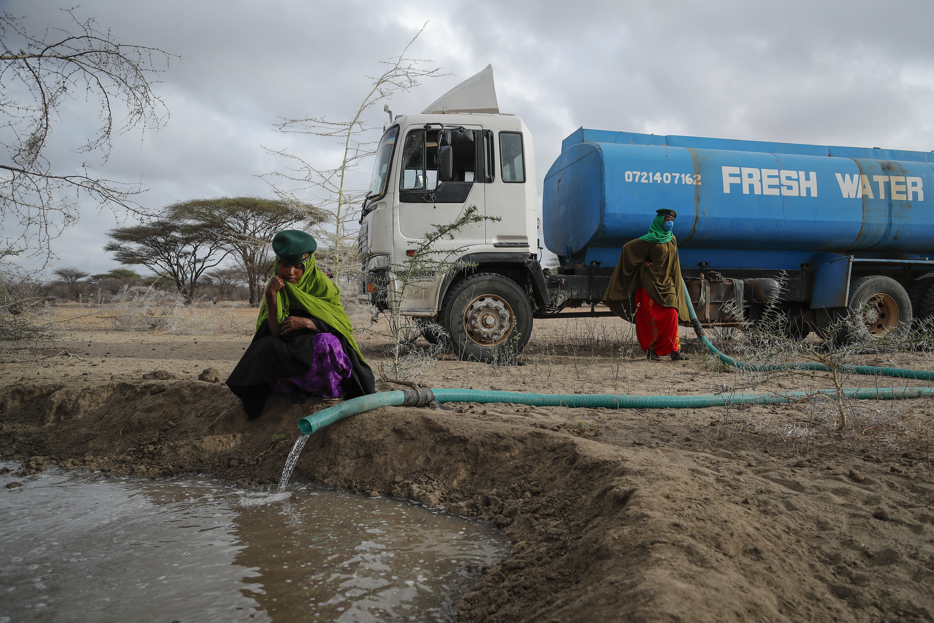 Two women guide a hose from a water truck filling up a dirt pool 