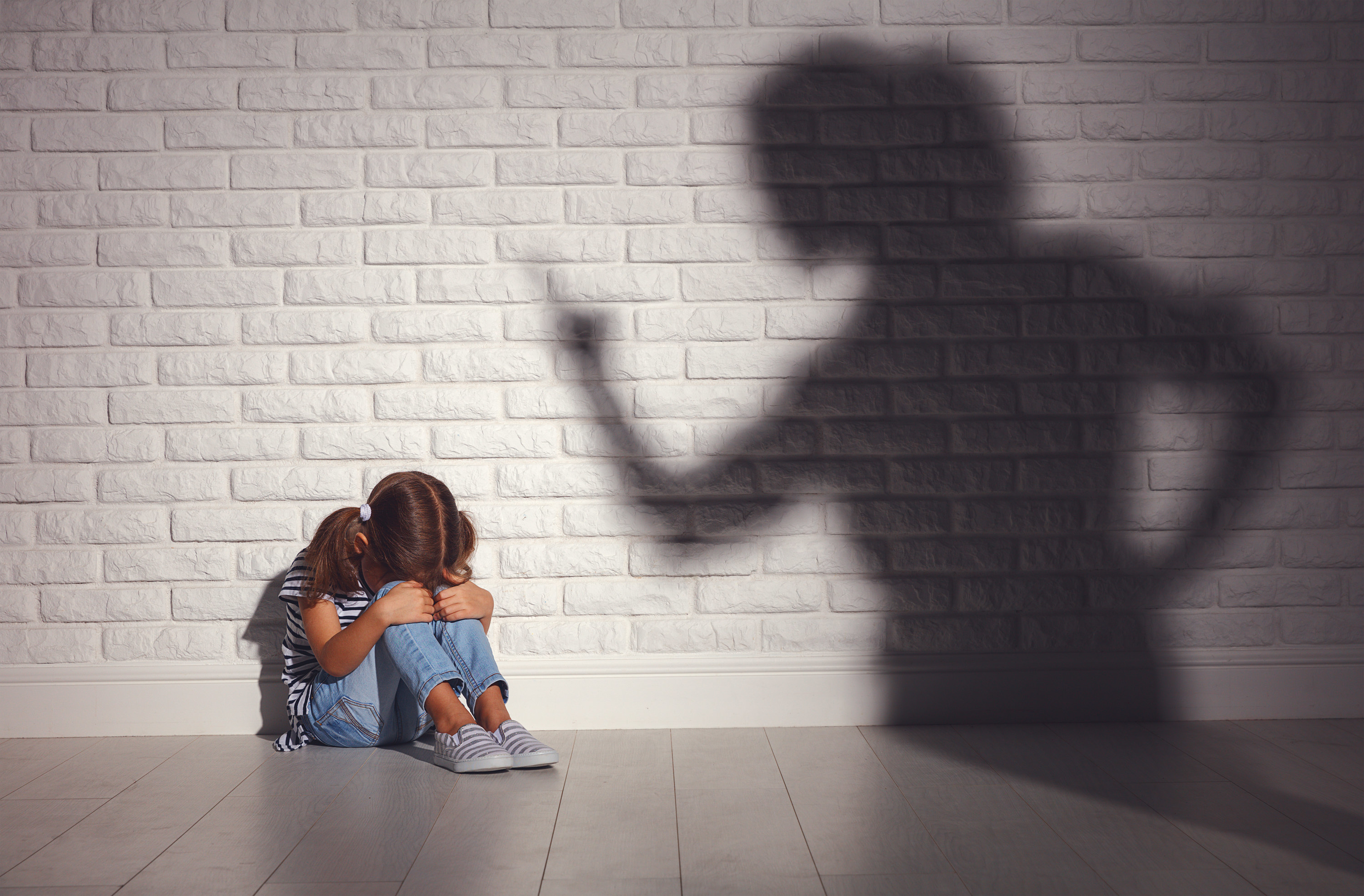 Little girl with her face in her knees in sadness with a shadow of her mother scolding her